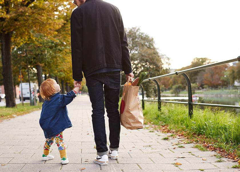 Pappa på promenad med sin dotter, hand i hand, med matkasse.