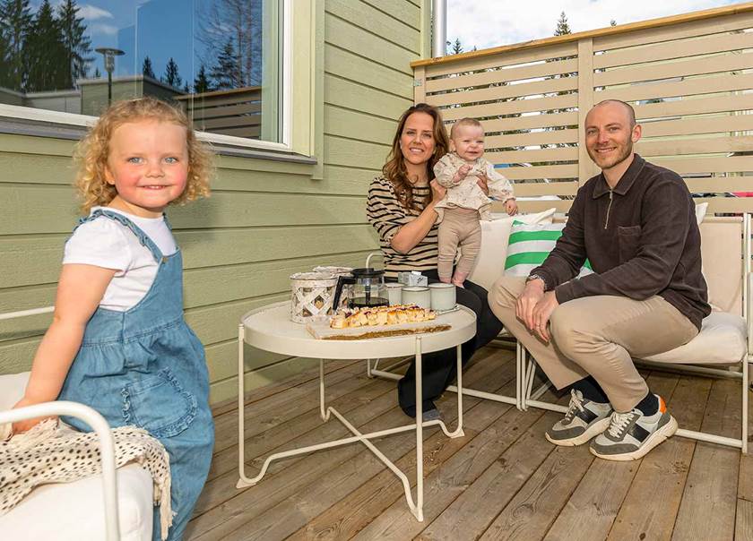 Liten flicka i jeanskläder framför mamma i brunt hår och beige tröja med i sparkdräkt och pappa i brun tröja och beige byxor. spädbarn 