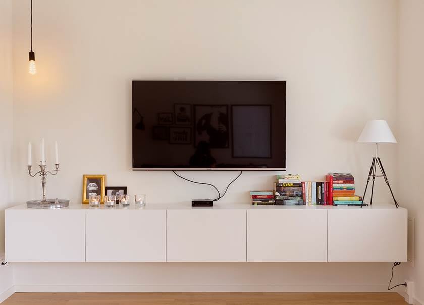 TV som hänger över TV bänk med lampa och böcker på