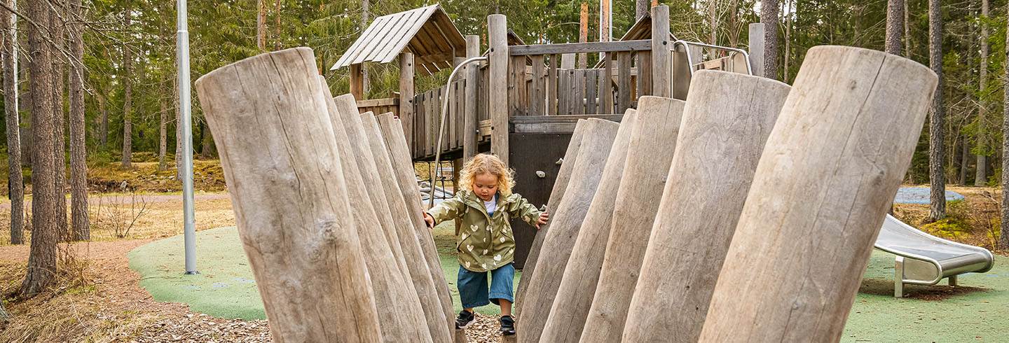 Flicka leker på lekplats och klättrar på stockar.n.