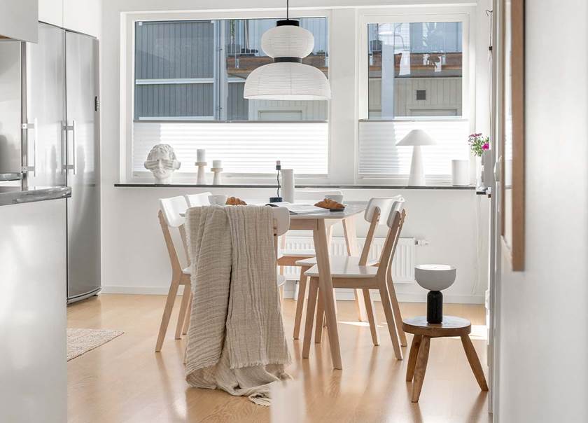 Två stora köksfönster lyser upp ett kök i vitt. På en köksstol hänger en ljusbrun filt.